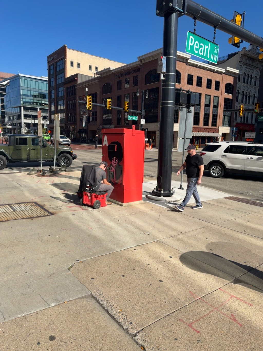 Red painted utility box with portrait artwork at Pearl Street in downtown Grand Rapids, with pedestrians nearby