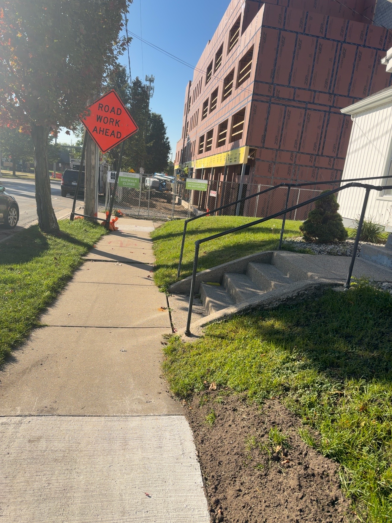 Road work sign beside a sidewalk and a building under construction.
