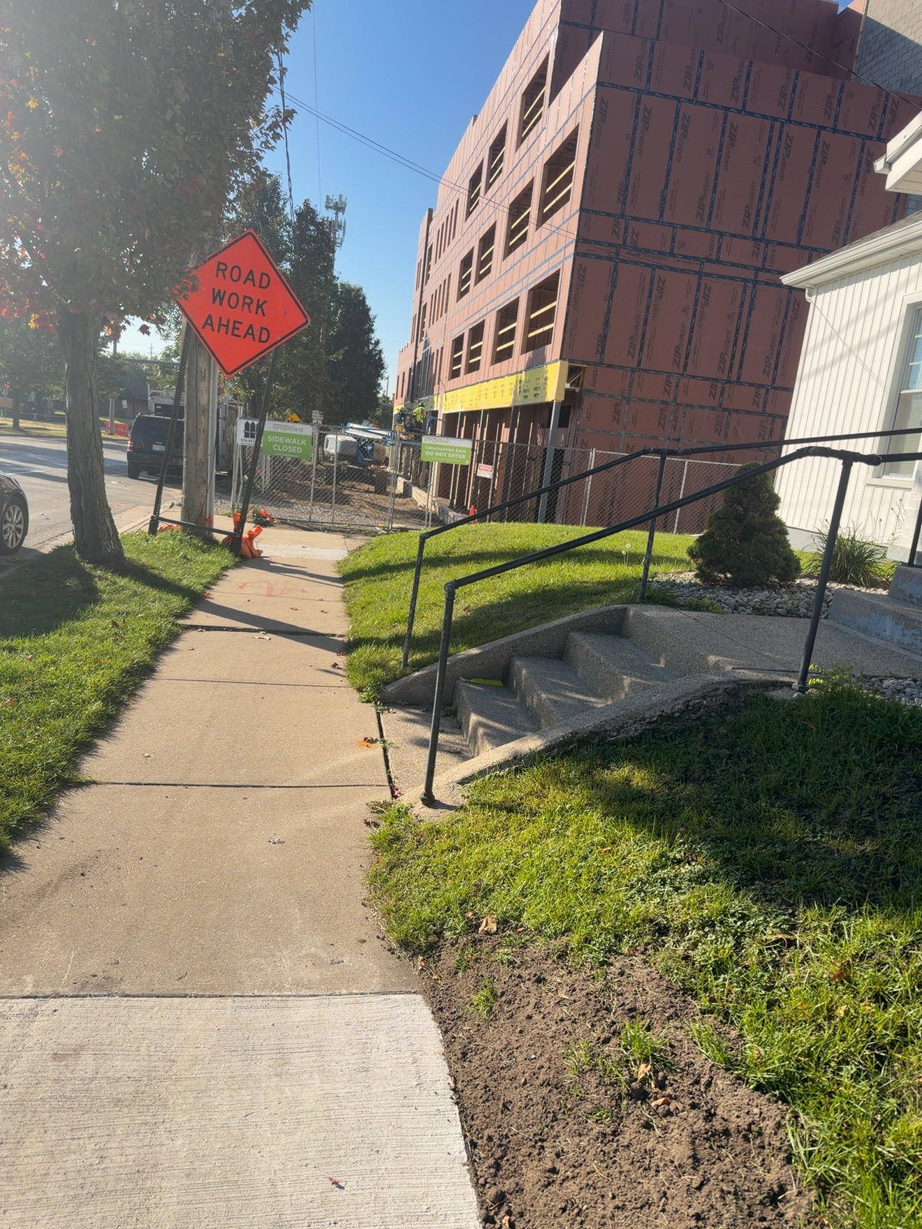 A sidewalk passes a road work sign and construction site.