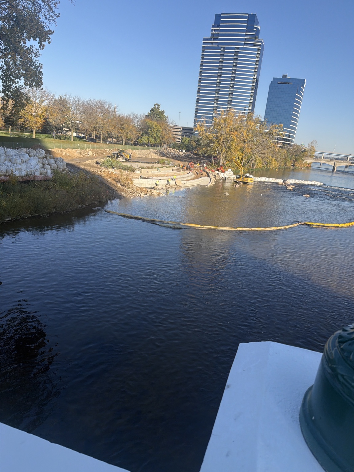 Riverfront earthworks, trees, a floating barrier, and a tall city building.